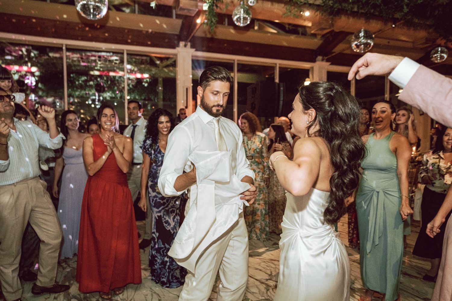 Bride and groom dance joyfully while guests clap and celebrate at wedding reception.