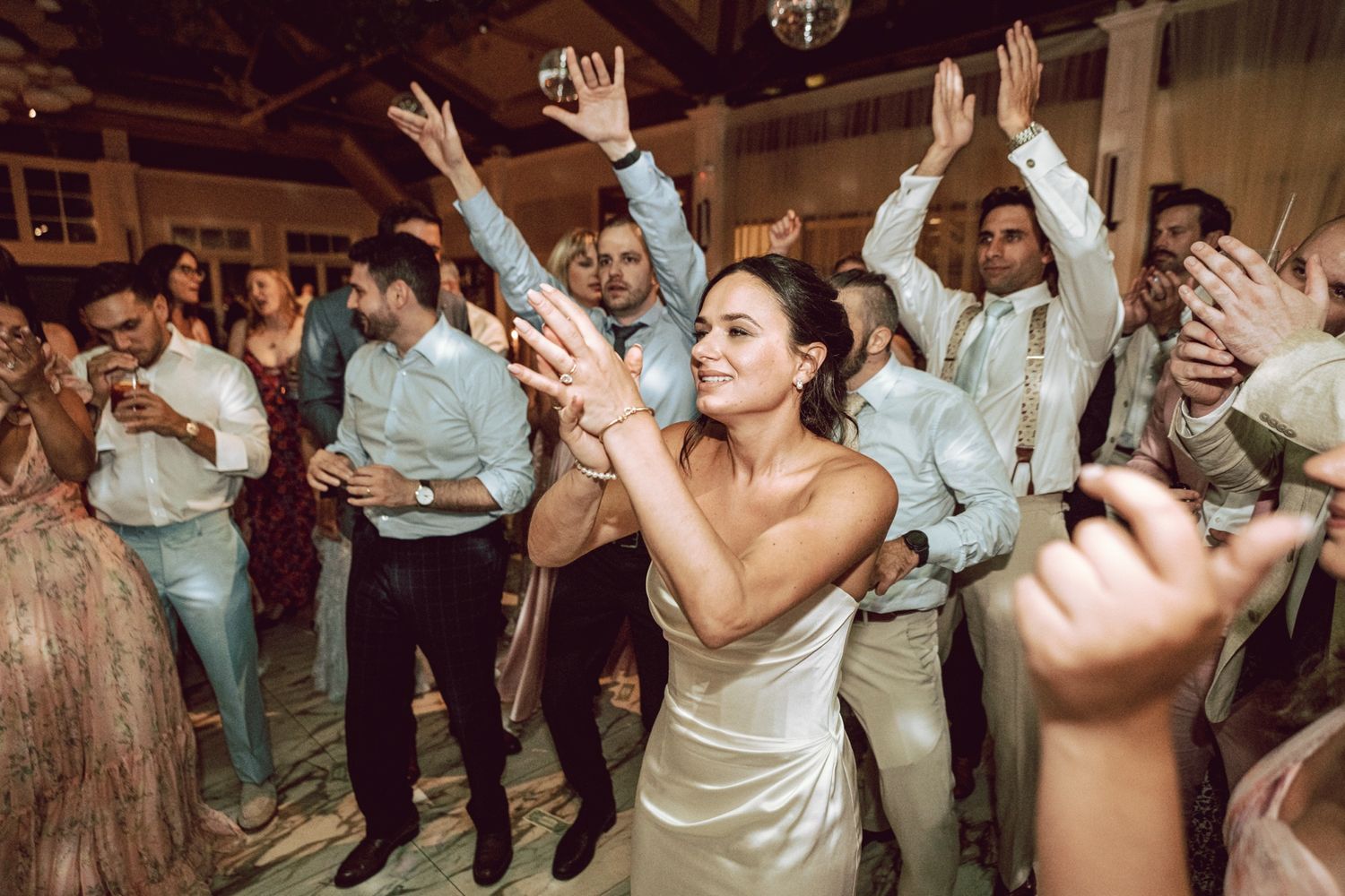 Bride in white gown dancing joyfully with guests at a lively wedding reception celebration.