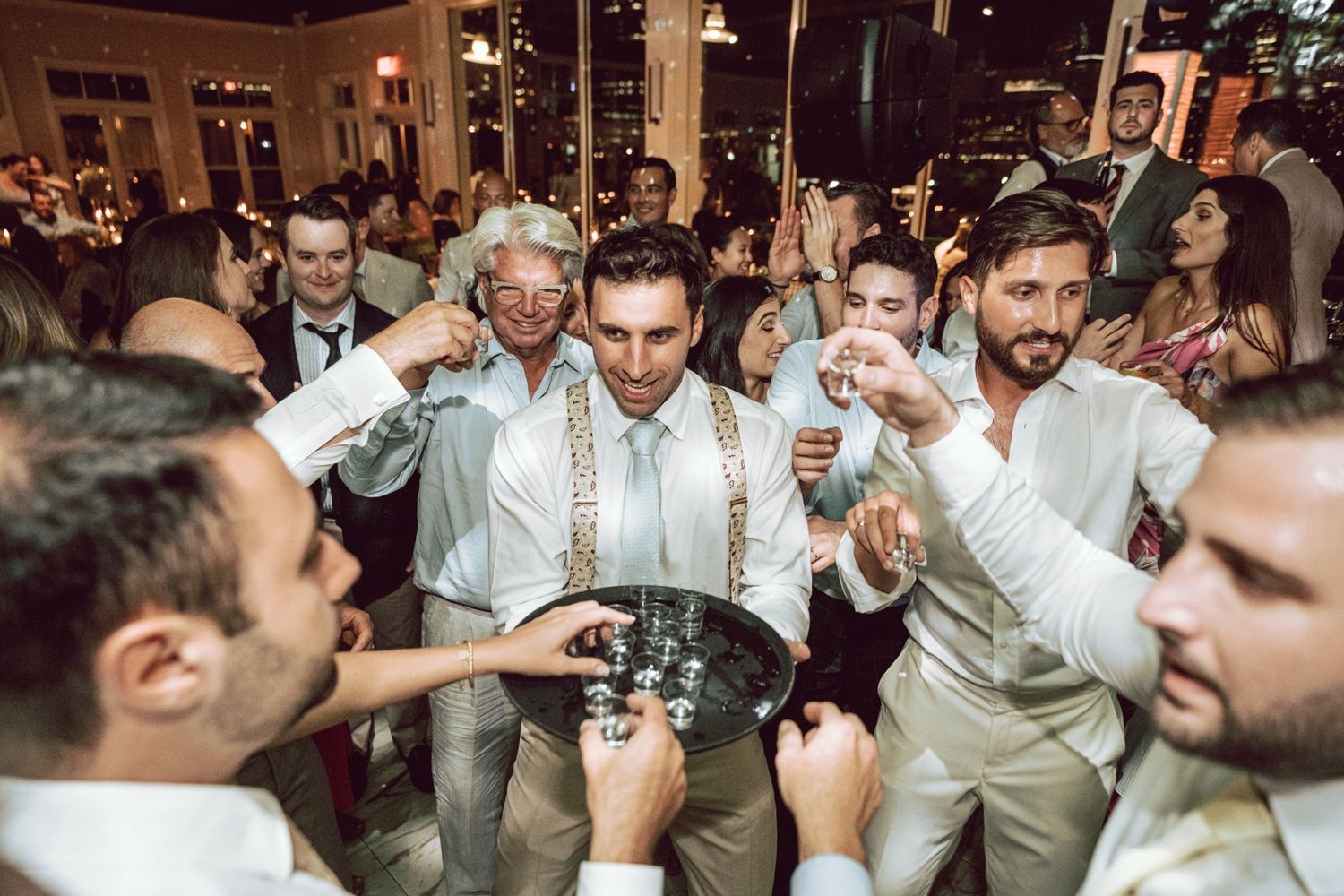Groom and groomsmen celebrate with shots on the wedding reception dance floor at night.