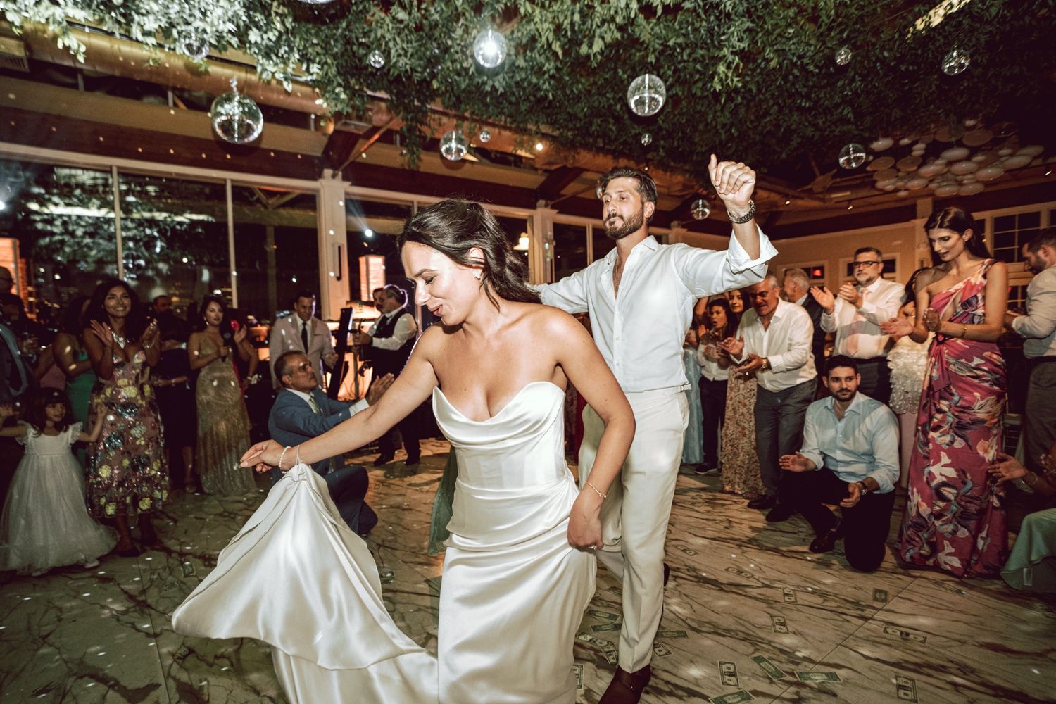 Bride and groom share first dance at elegant outdoor wedding reception with guests watching.