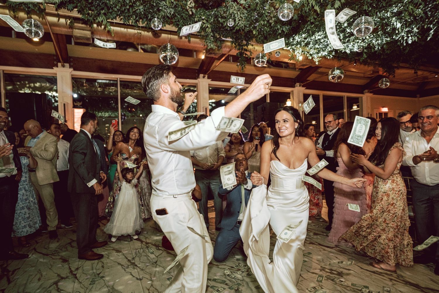 Bride and groom dancing joyfully at outdoor wedding reception surrounded by cheering guests under pergola lights.