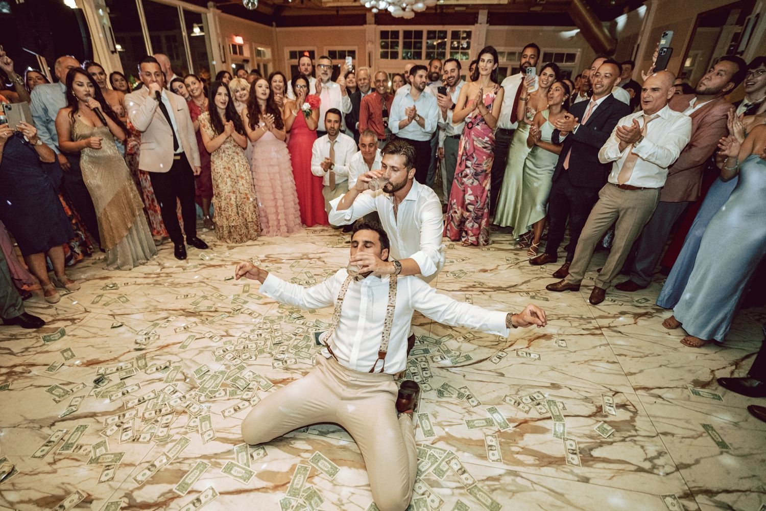Groom dramatically kneels on dance floor during lively wedding reception celebration with guests.
