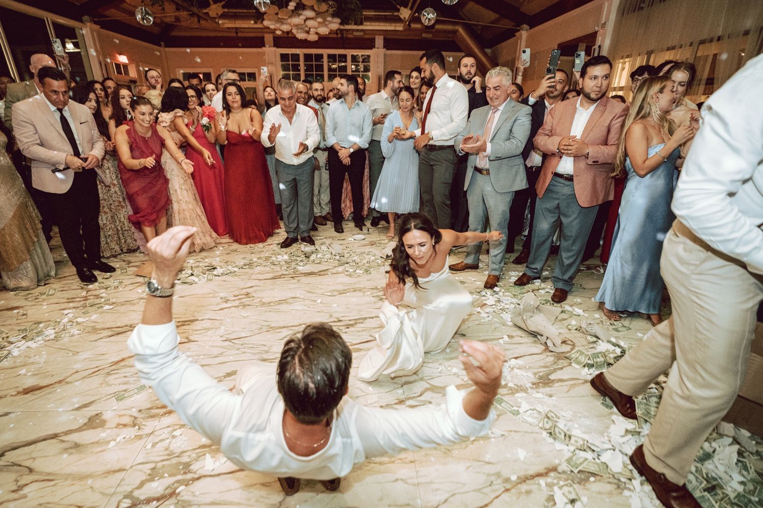 Groom dancing energetically on wedding reception dance floor surrounded by cheering guests.