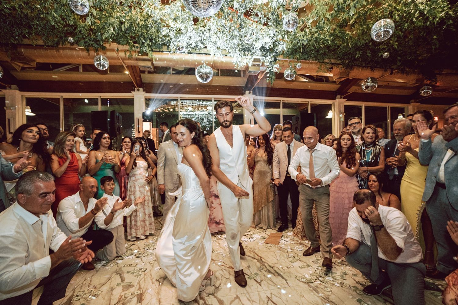 Bride and groom celebrate joyfully on confetti-covered dance floor at wedding reception.