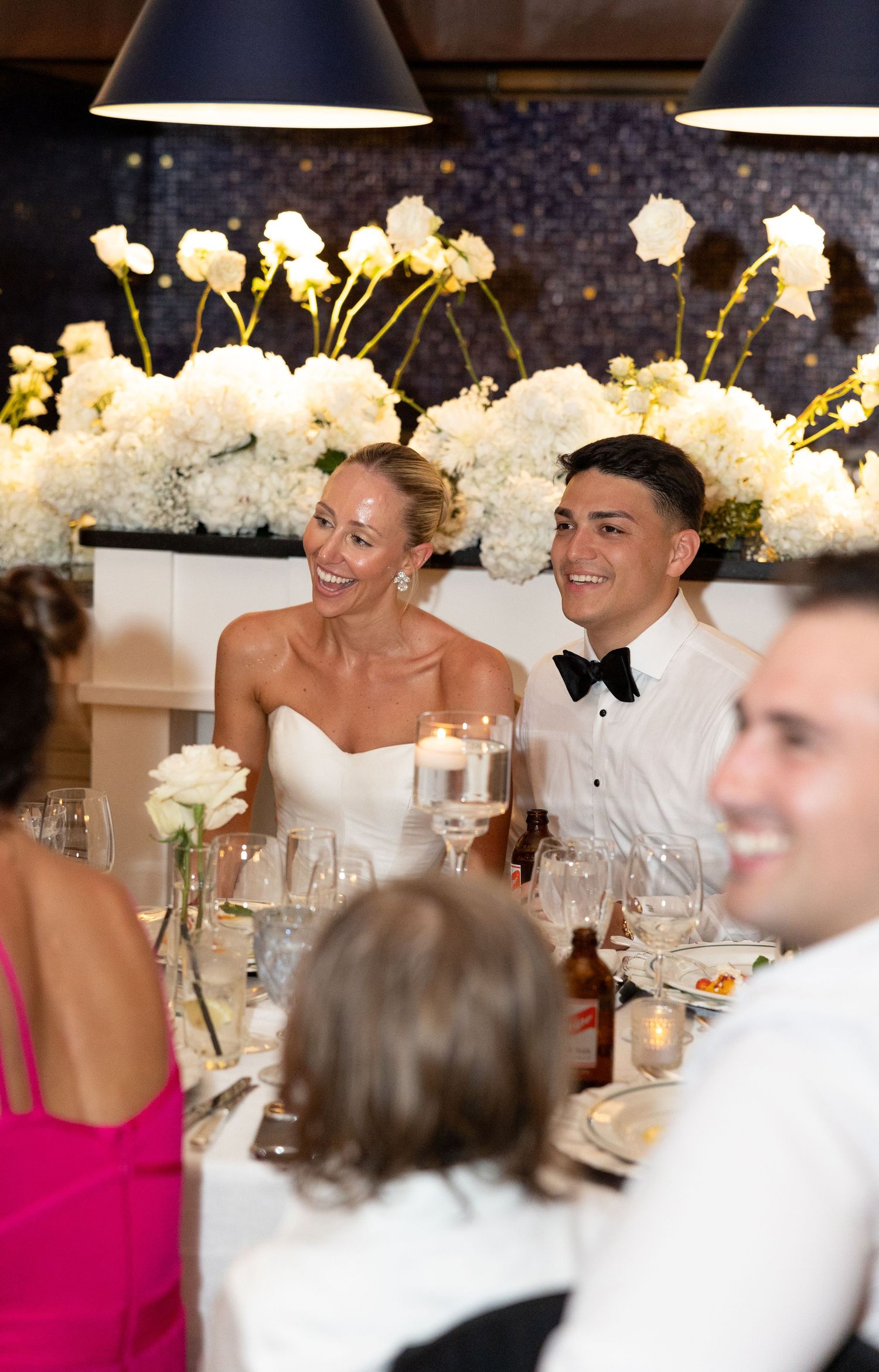 Bride and groom walk hand-in-hand down candlelit steps at night, woman in white gown raising her hand.