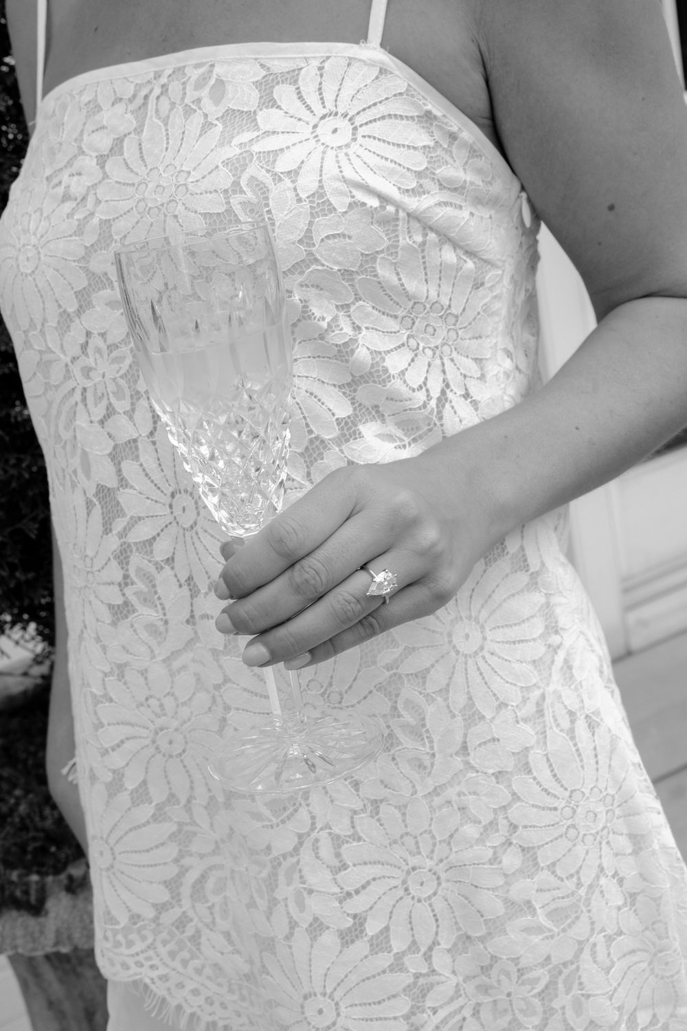 Close-up of a bride in a white lace dress displaying her diamond engagement ring.