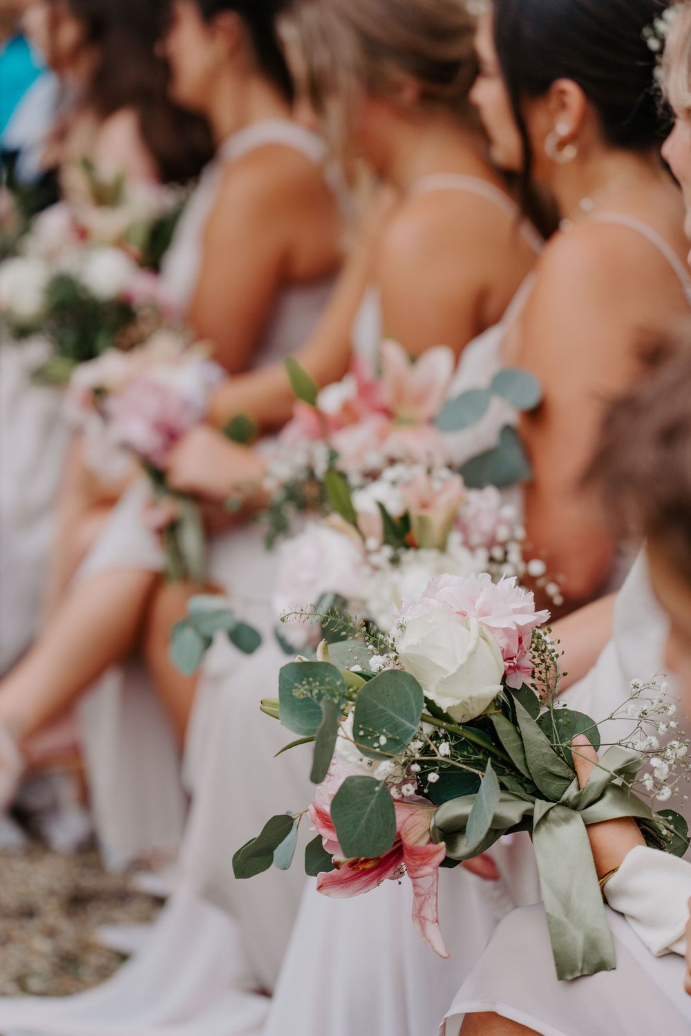 Bridesmaids in white dresses holding bouquets of pink flowers, eucalyptus, and baby's breath at a wedding ceremony.