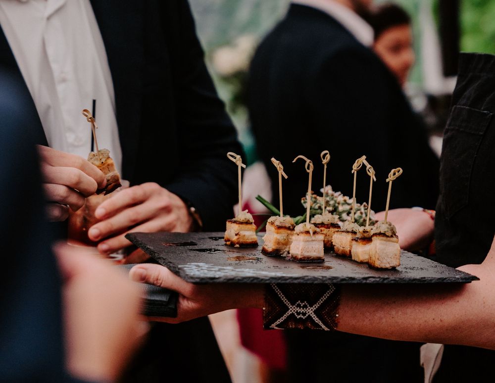 Guests enjoying gourmet bite-sized appetizers served on a slate board at an upscale catering event.