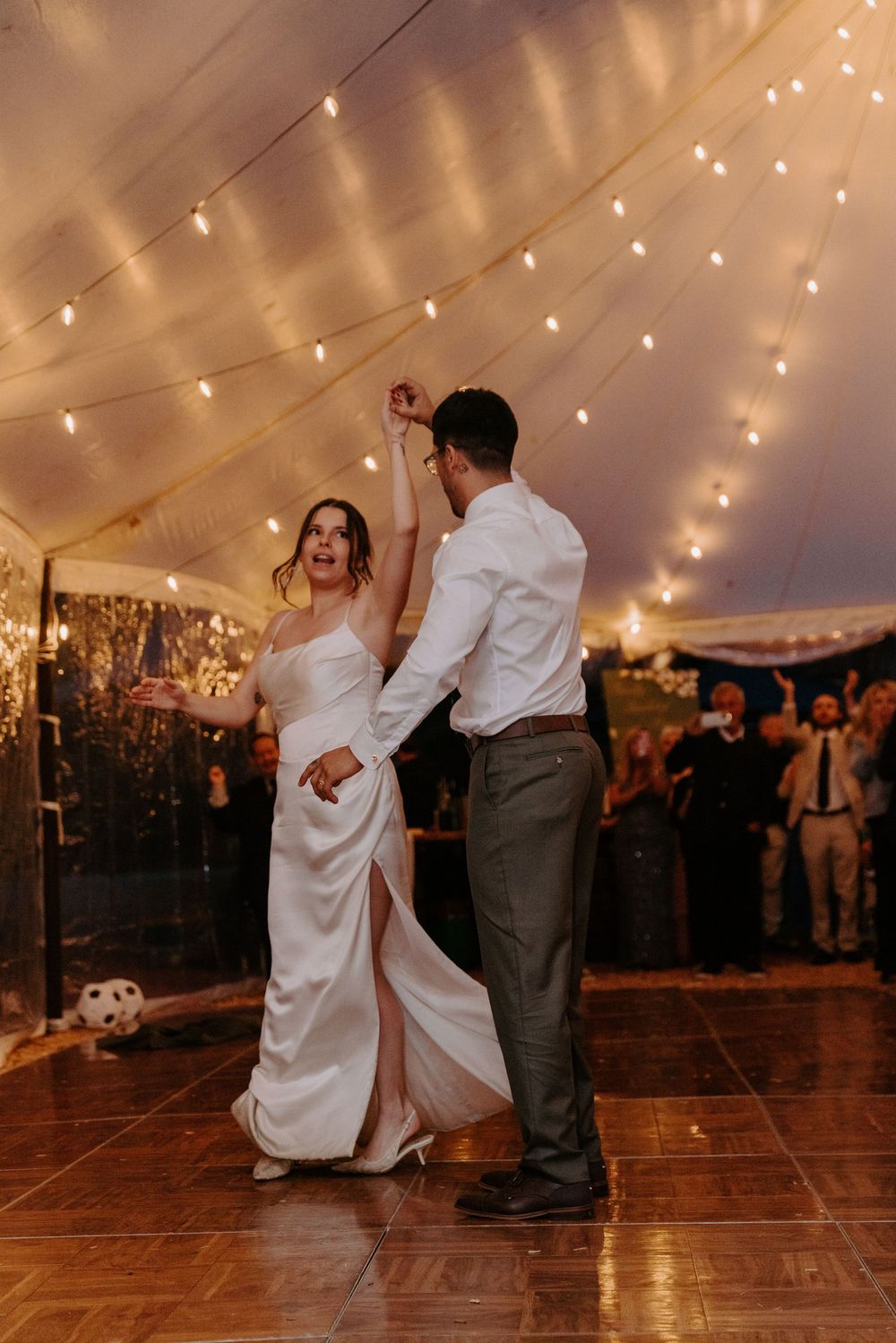 Bride and groom share first dance under twinkling string lights in a romantic wedding tent reception.