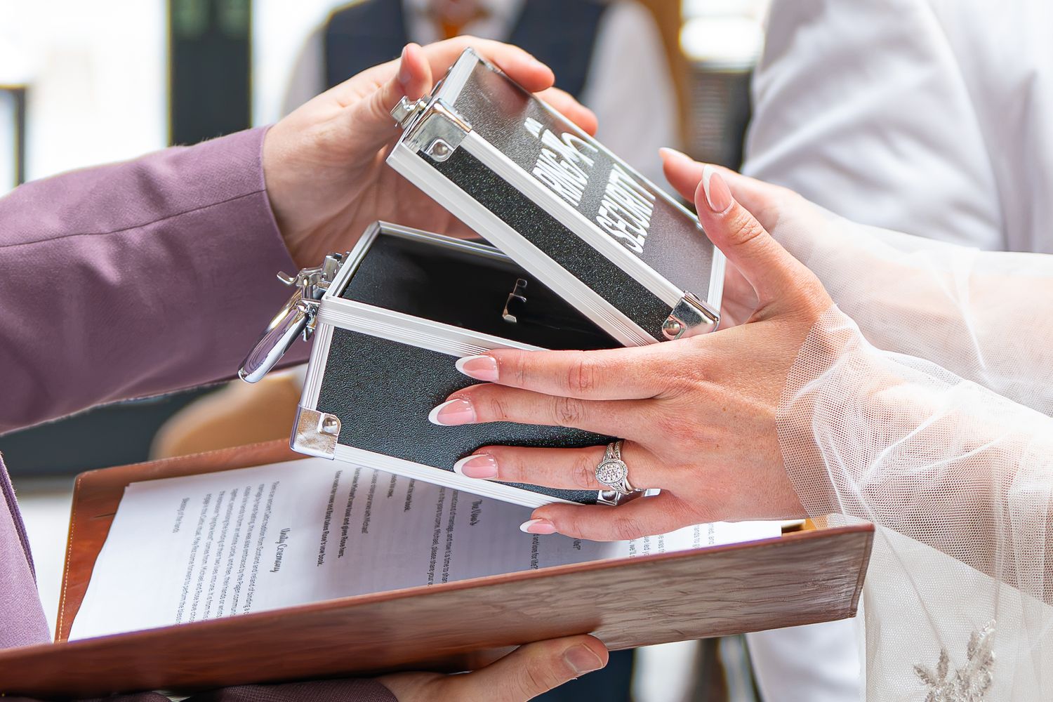 Close-up of hands exchanging a ring box at a wedding ceremony, with signed documents visible below.Yorkshire, Sheffield, Lincolnshire, UK