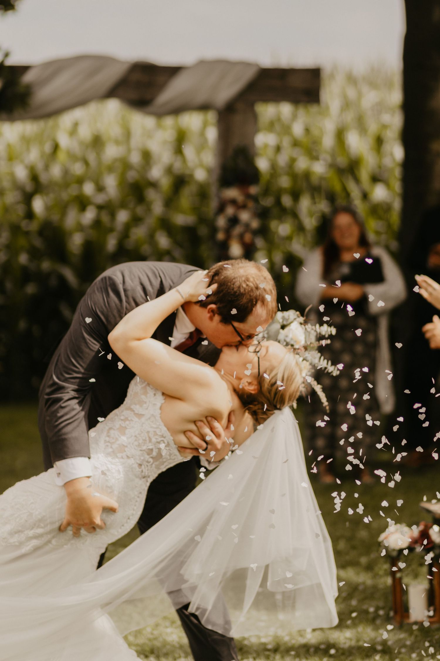Dramatic wedding dip kiss with confetti flying in garden setting.