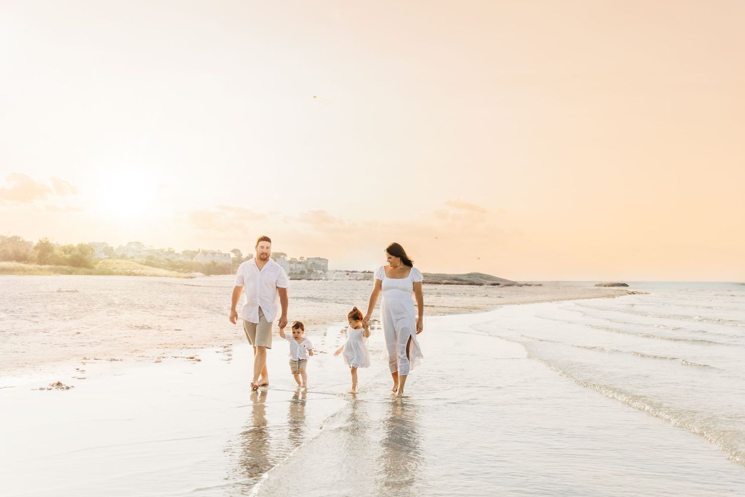 A family walks together along a peaceful beach at sunset with waves lapping at their feet.