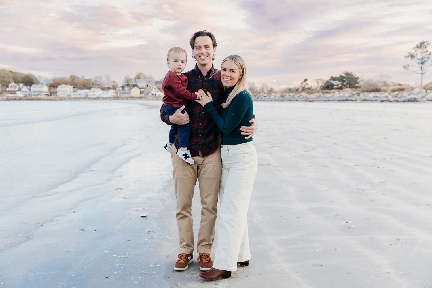 A family in casual attire stands together on a snowy winter landscape with houses visible in the distance.