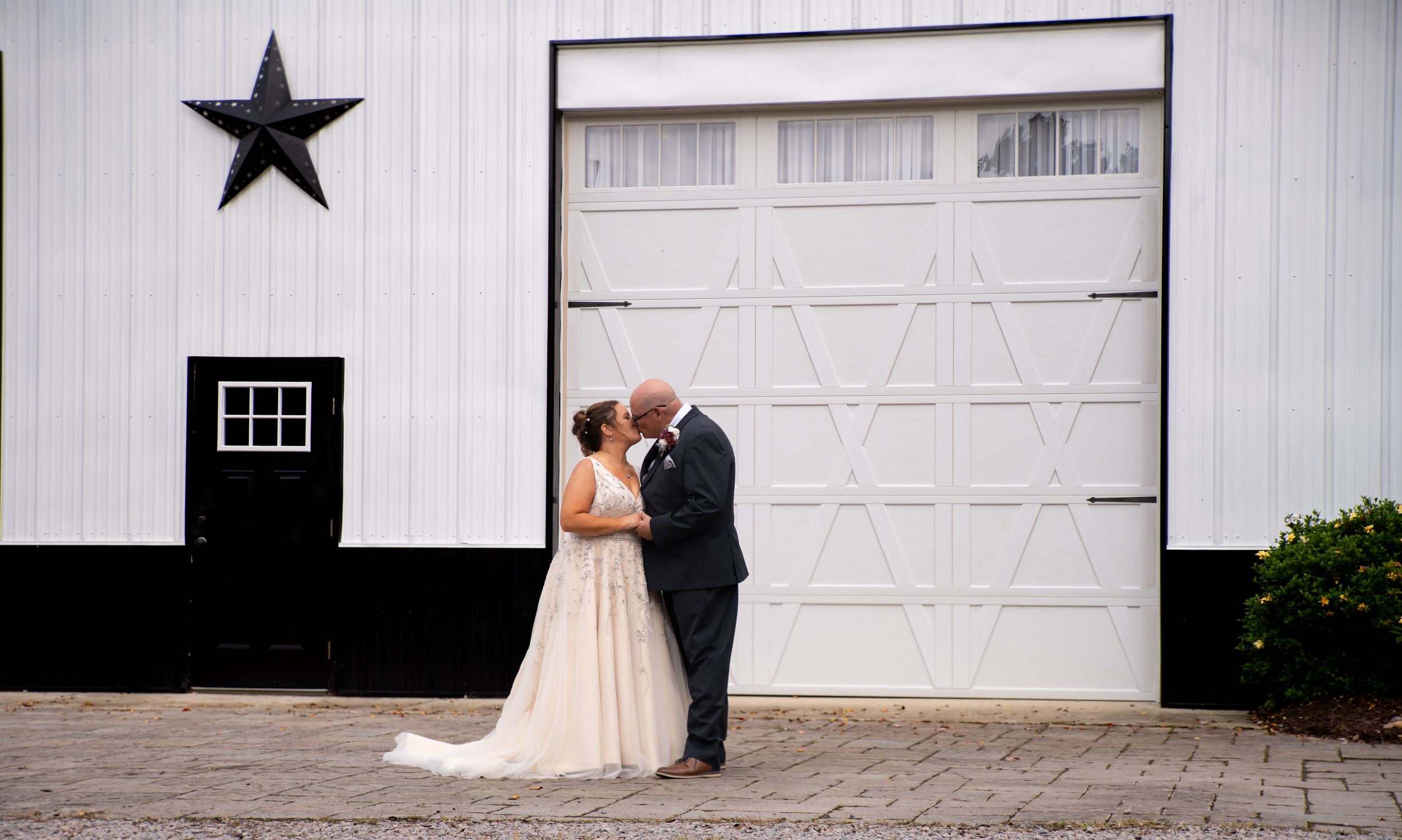 Wedding portrait in front of a white barn with black trim and decorative star.
