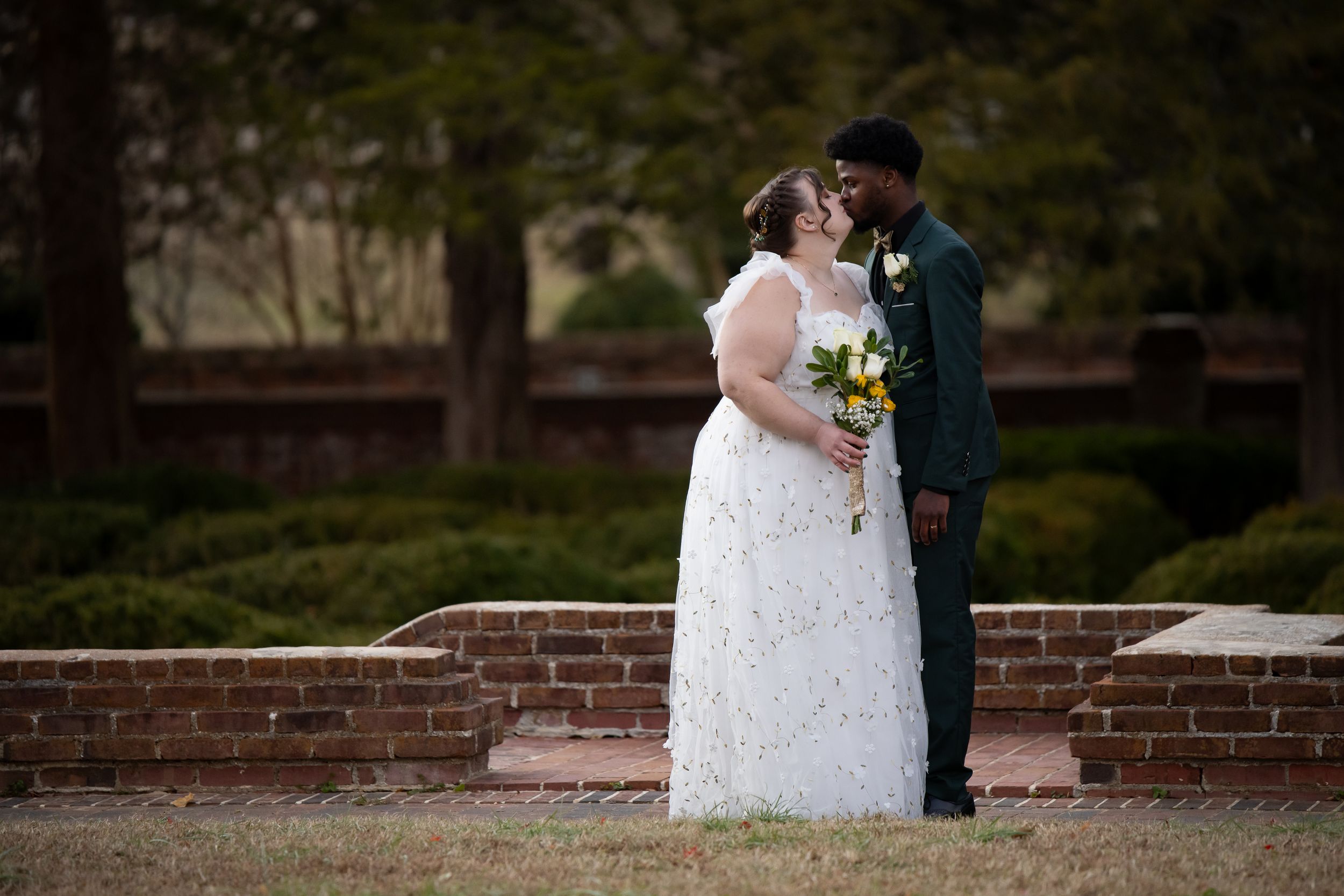 A couple shares an intimate moment in front of a brick wall at their outdoor wedding ceremony.
