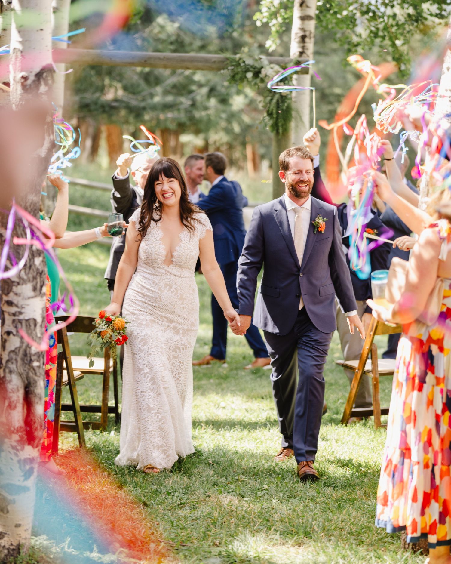 Wedding ceremony exit with colorful streamers and rainbow lens flare in outdoor garden setting.