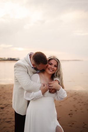 A tender moment between a couple in white outfits on a beach at sunset.