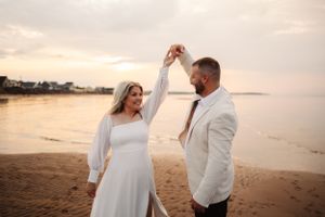 A couple shares playful moments on a sandy beach during golden hour.