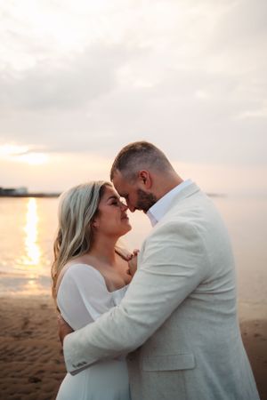 An intimate sunset beach portrait of a couple in coordinating white outfits.