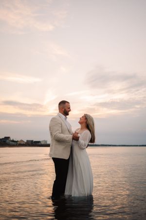 A couple stands in ocean water during sunset for a romantic photoshoot.