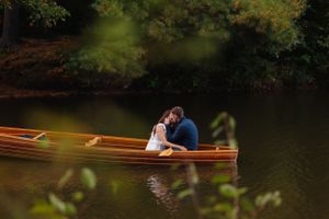 A wooden boat floats peacefully on calm waters under autumn trees.