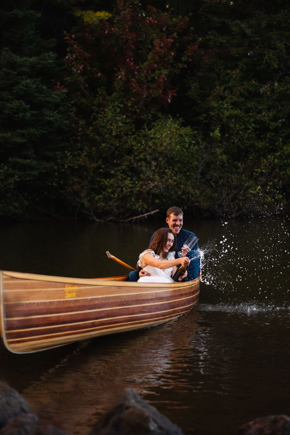Couple embracing in wooden canoe surrounded by autumn trees and dark water.