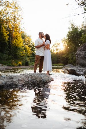 Romantic couple embracing on rocks over reflective river water at sunset.
