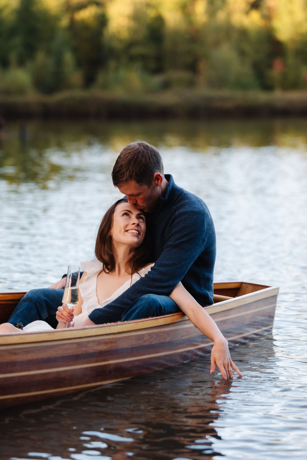 Couple sharing tender moment while relaxing in wooden canoe on calm lake.