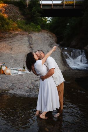 A romantic couple shares an intimate moment while standing in a creek with a waterfall in the background.