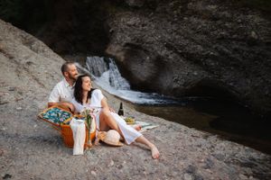 A couple lying together on rocks by a scenic creek during an outdoor photoshoot.