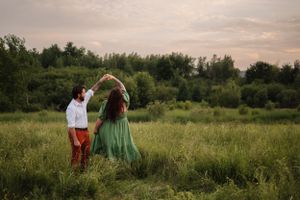 Couple dances playfully in a green field during sunset with trees in background.