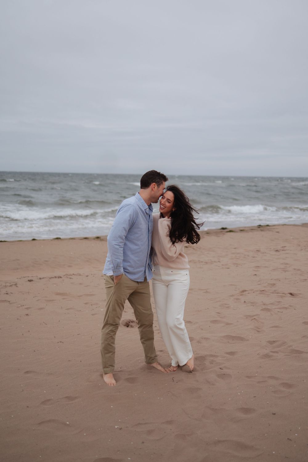 A romantic couple shares an intimate moment while dancing on a cloudy beach.