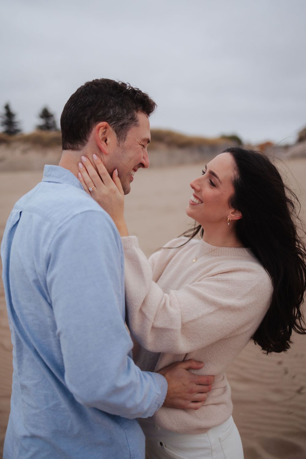 A couple shares a joyful moment together on sandy dunes by the ocean.