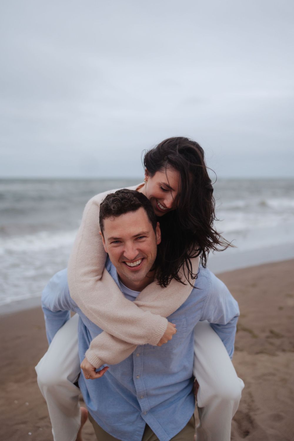 A couple laughs while sharing a piggyback ride on a beach.