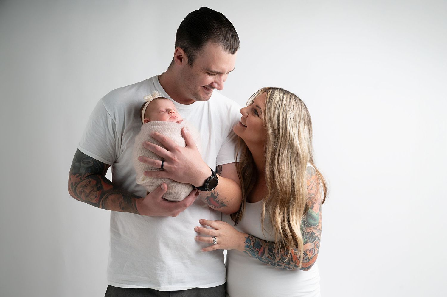 Couple sharing intimate moment with newborn baby against white background in studio.