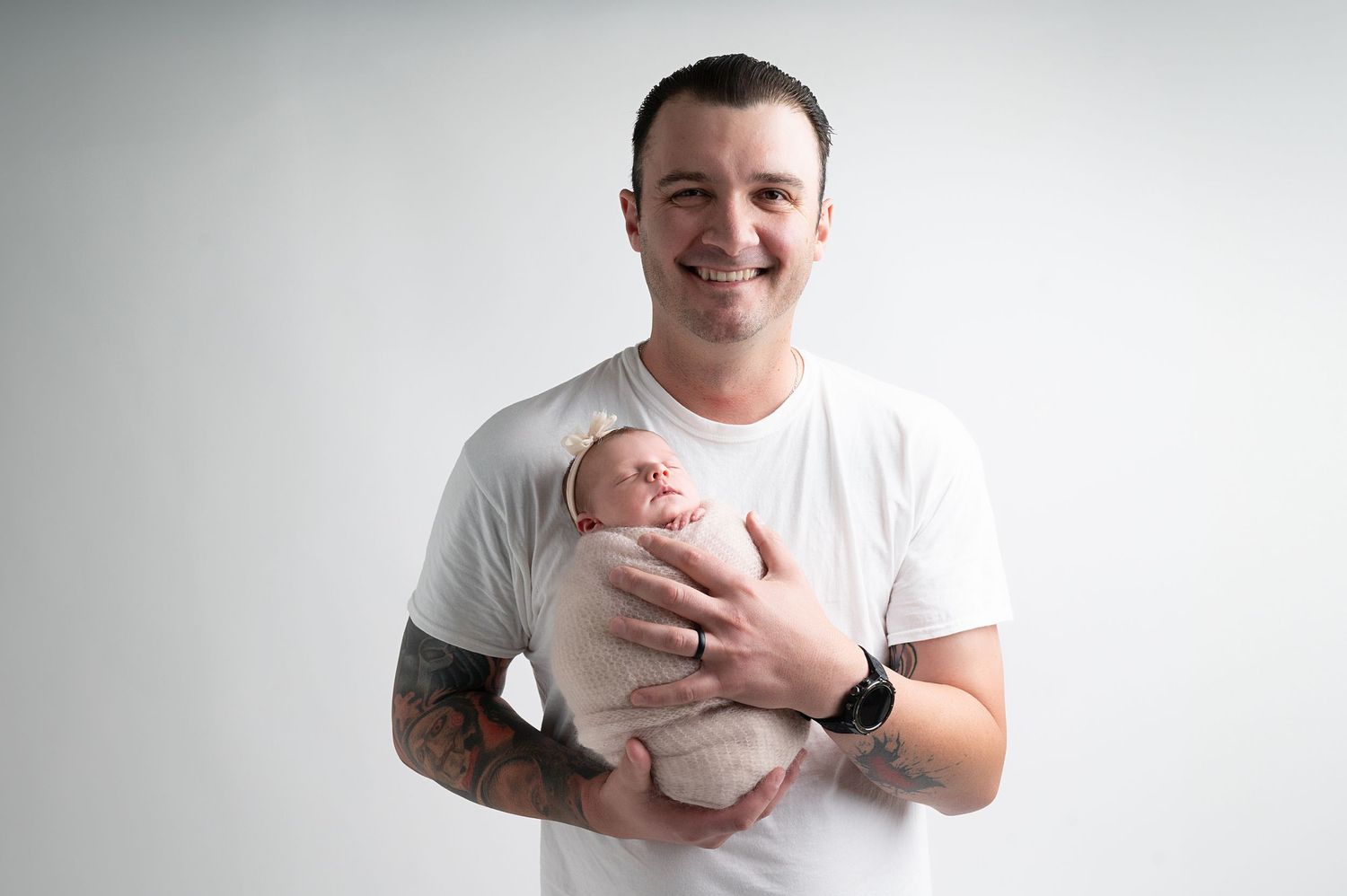 Parent in white t-shirt holding newborn baby against neutral background in studio setting.