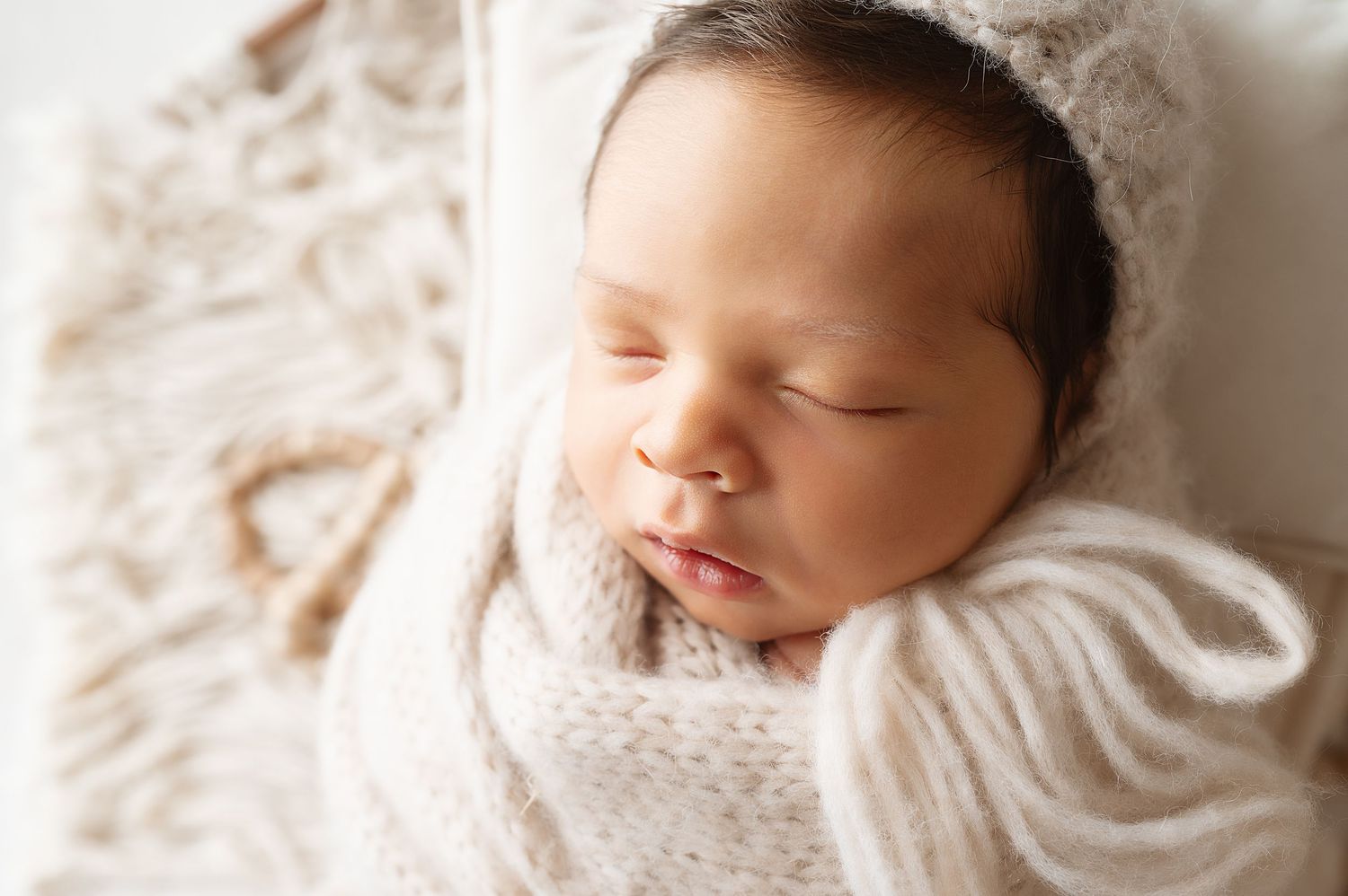 Peaceful newborn sleeping while wrapped in soft white blanket during professional photo session.