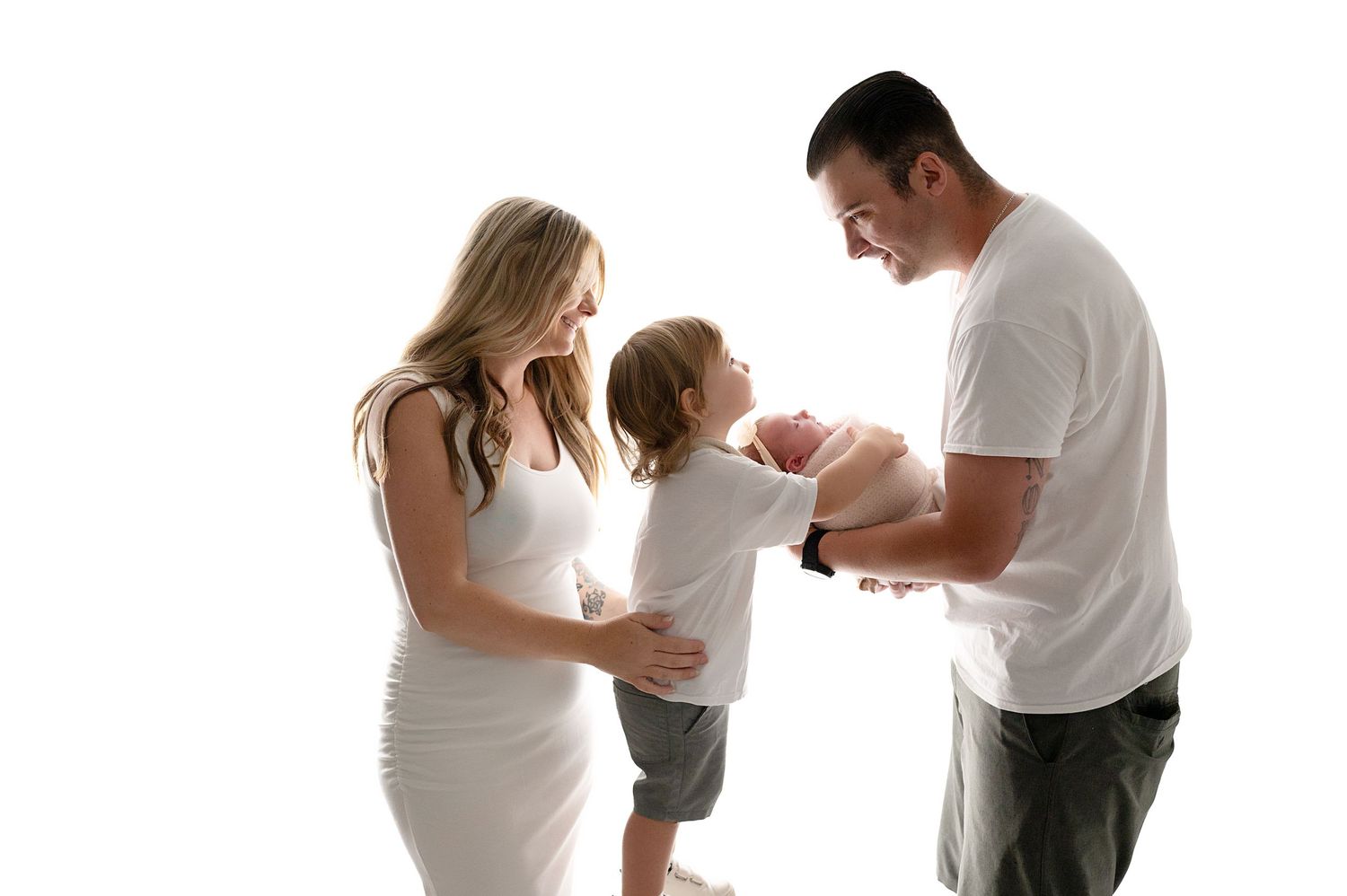 Family of three in white attire sharing intimate moment against light background.