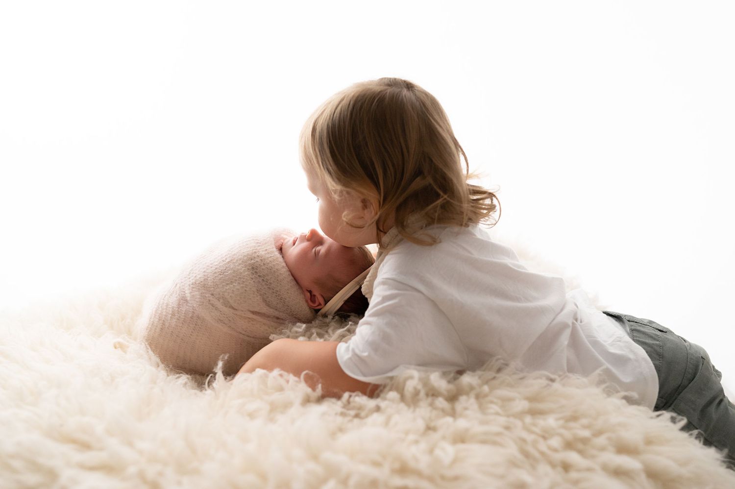 Two siblings sharing a tender moment on fluffy white rug.