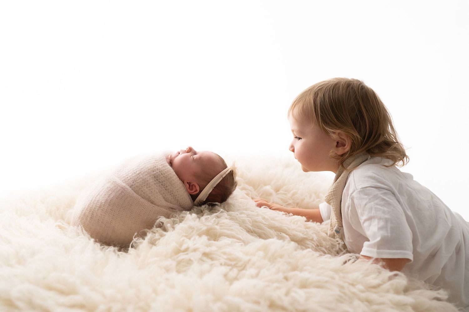 Sweet interaction between siblings on soft cream colored fur rug.