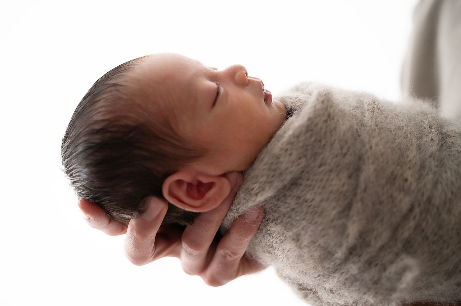 Close-up of tiny sleeping newborn being gently cradled in hands.