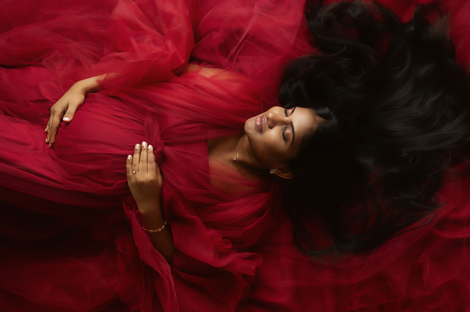 Woman in flowing red dress lies dramatically against red fabric backdrop.