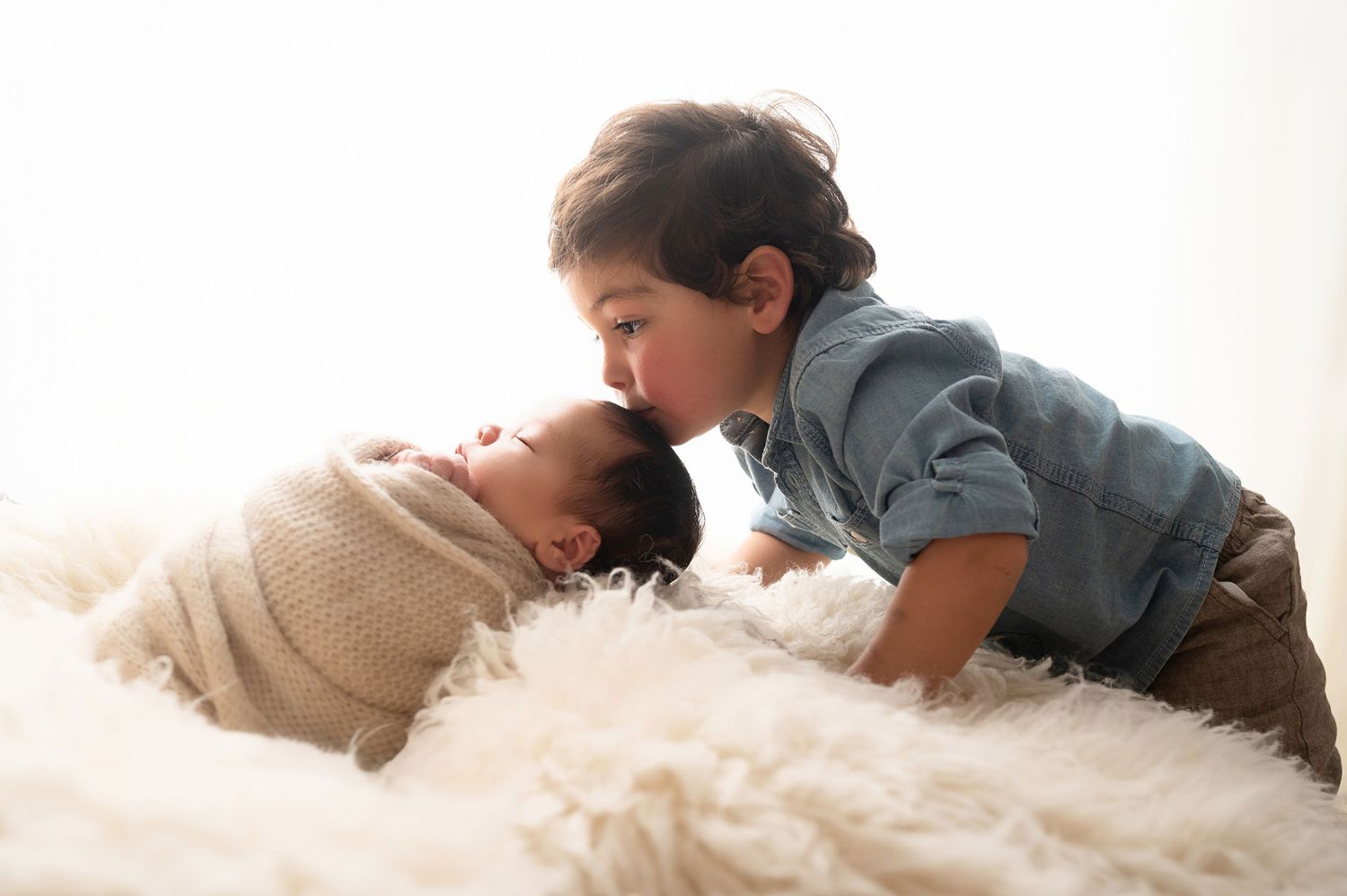 Sibling interaction captured in soft lighting on white fluffy backdrop during photo session.