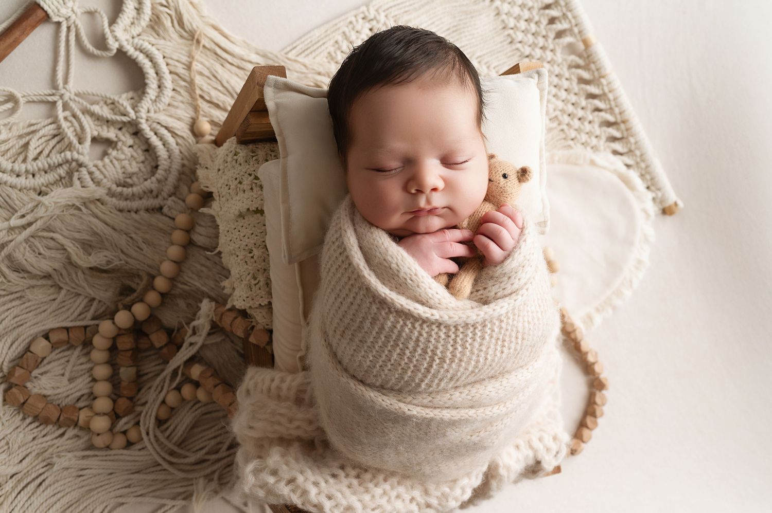 Baby resting in cozy cream-colored knit wrap on white backdrop.