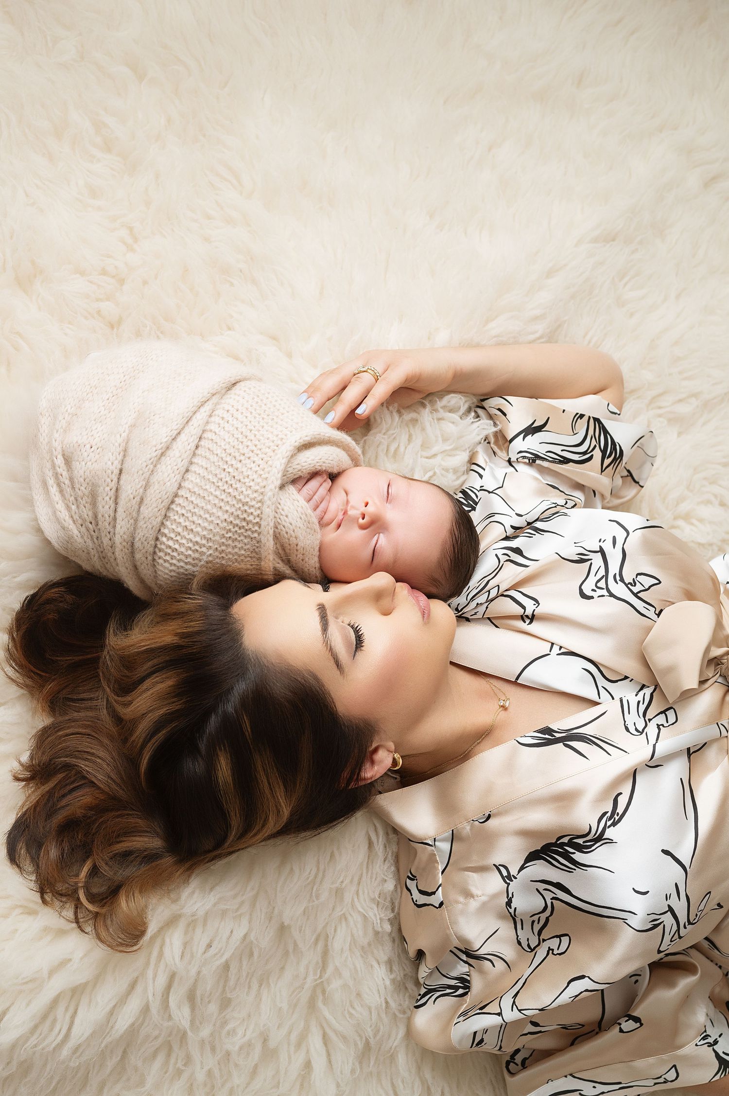 Woman in patterned dress lying on plush white rug during maternity photoshoot.