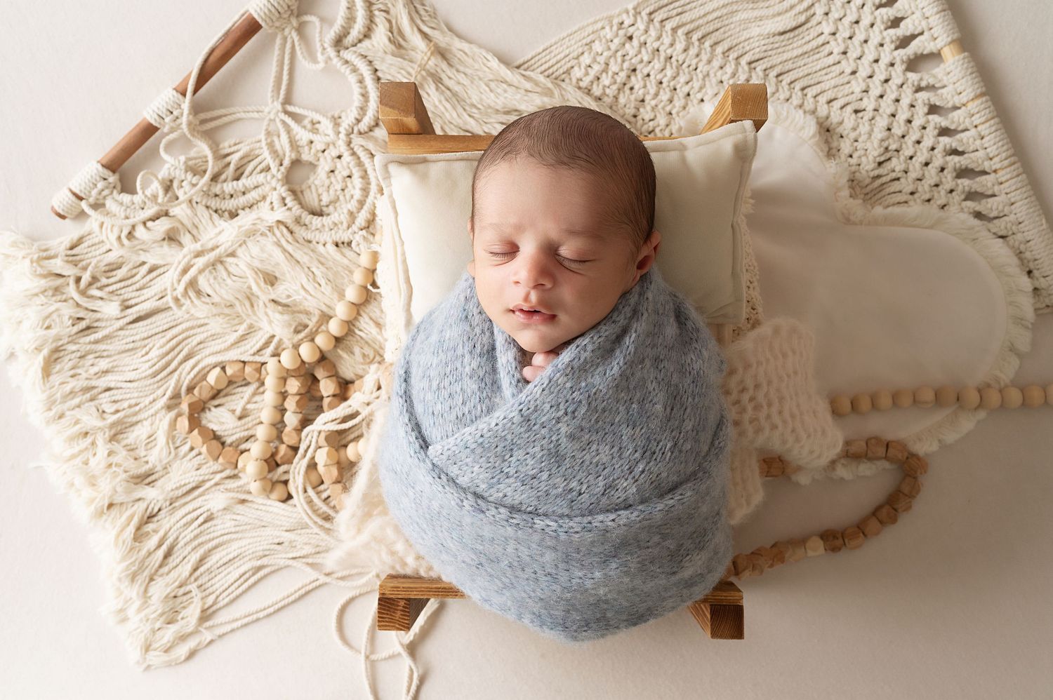 Baby sleeping peacefully in gray wrap on cream textured background.