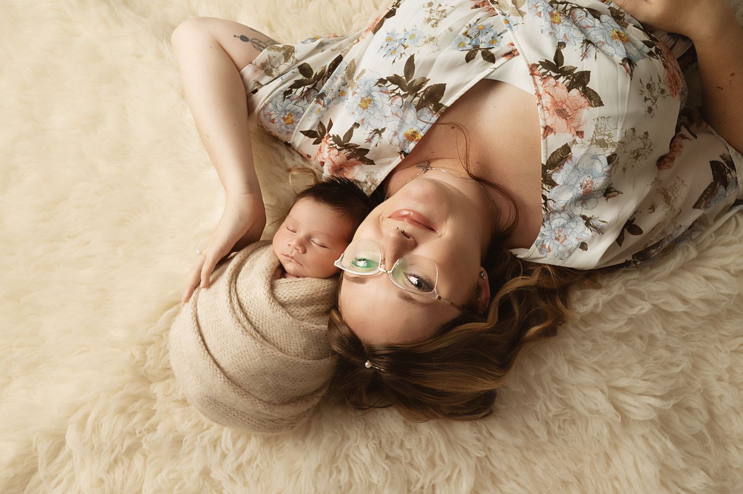 Mother and newborn baby lying on cream carpet during intimate portrait session.