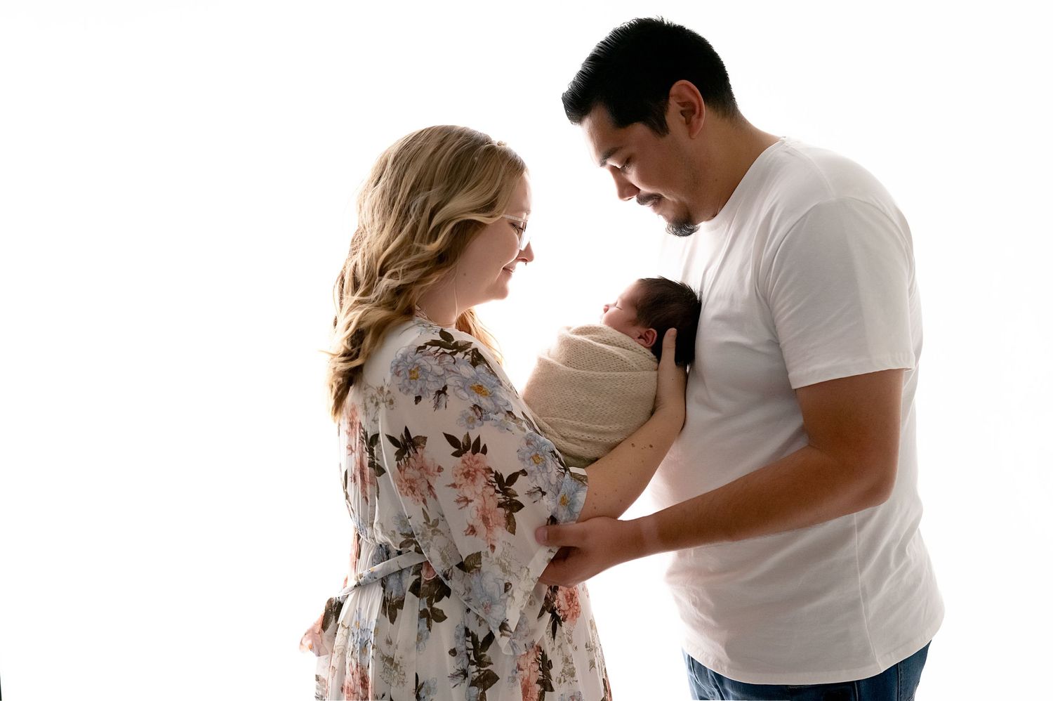 Parents gazing lovingly at newborn baby between them in soft studio lighting.