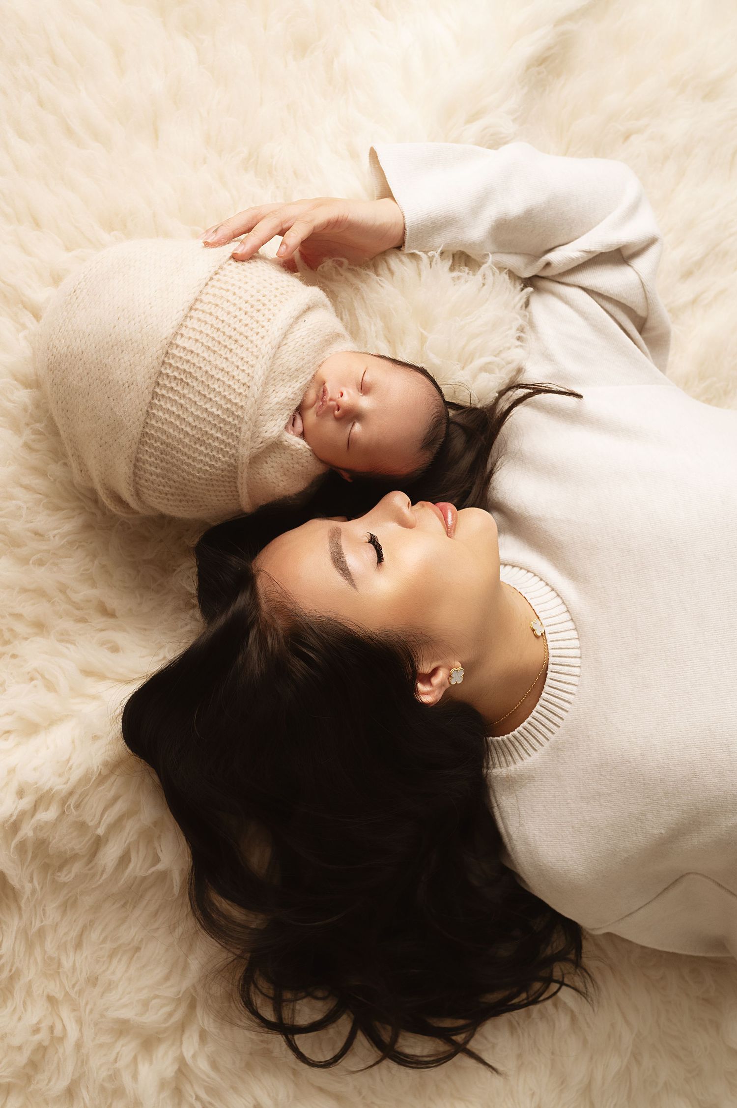 Parent and child in matching white sweaters lying on plush cream rug during intimate portrait session.