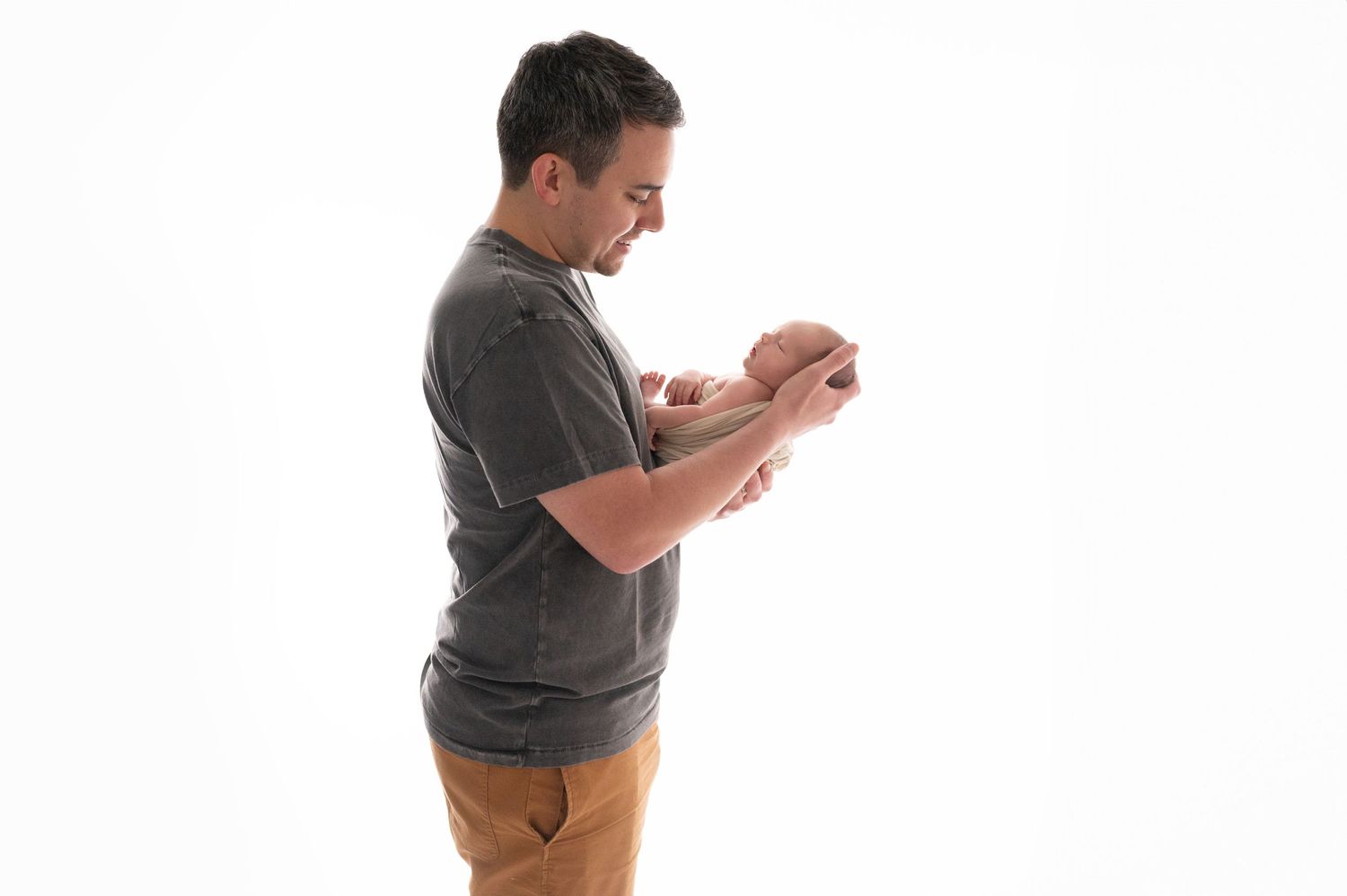 A person holds a swaddled newborn baby against a white background.